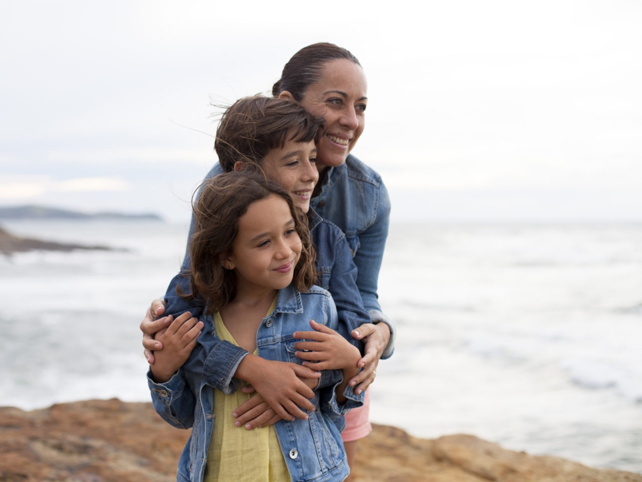 Madre abrazando a sus hijos junto al mar